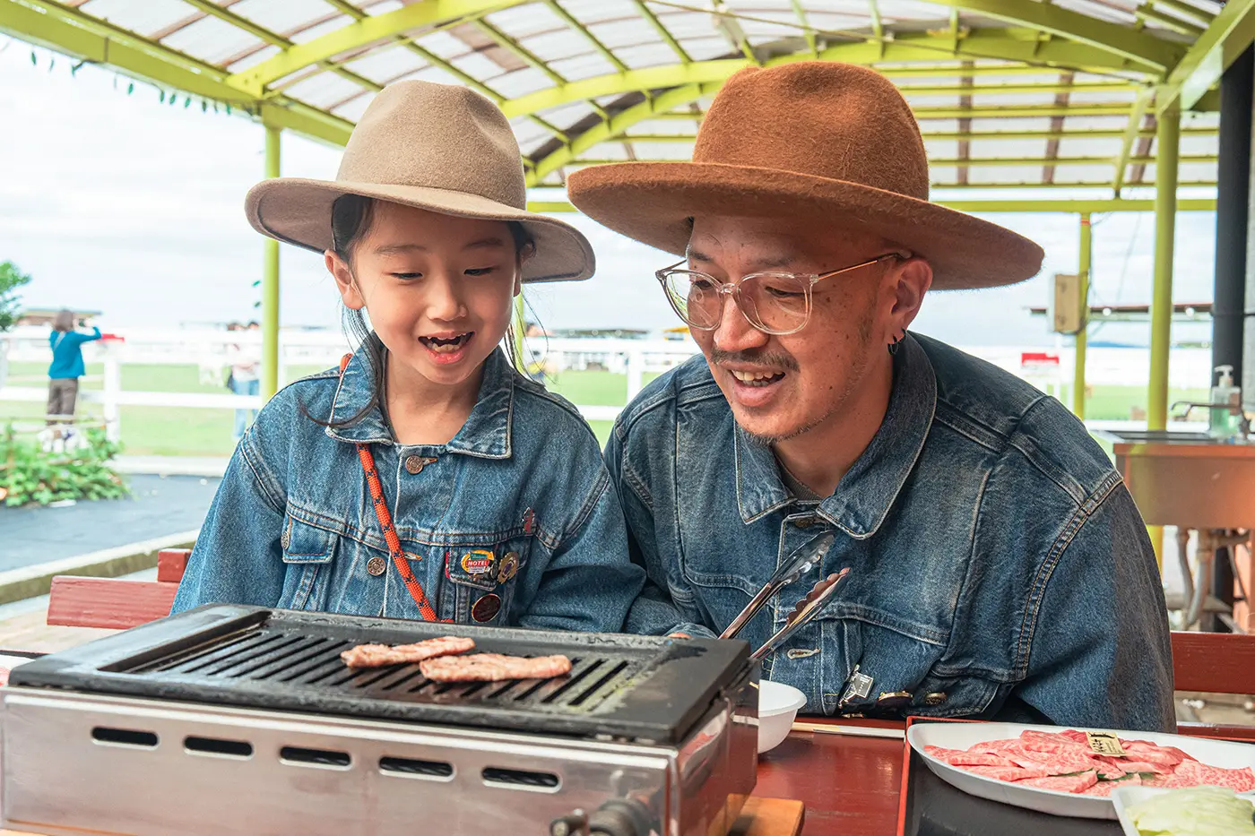 A parent and child grilling meat at a BBQ